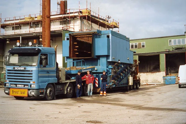 Blå Scania lastad med en stor industrimaskin utanför en fabrik