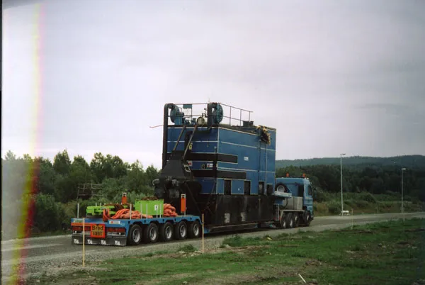 Ekipage med en stor maskindel på lång trailer längs en landsväg